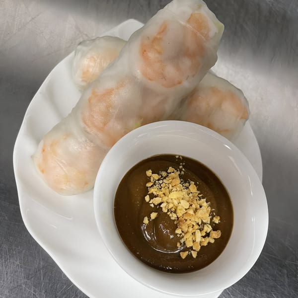 Three fresh spring rolls with shrimp and a side of peanut dipping sauce topped with crushed peanuts.