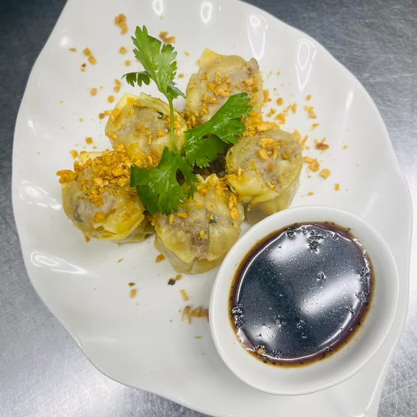 Five Thai dumplings topped with crispy garlic and cilantro, served with a side of dark dipping sauce.
