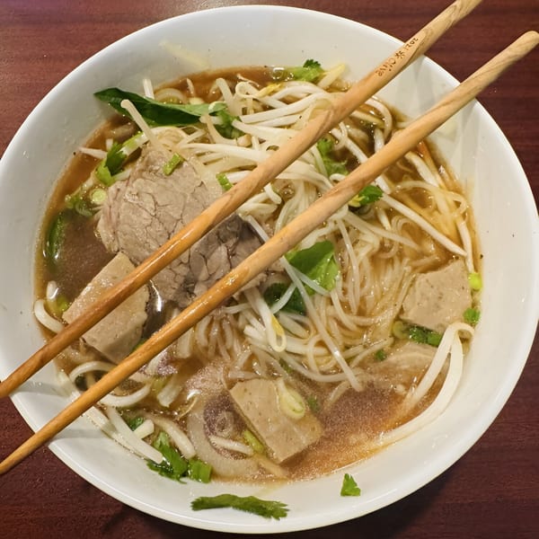A bowl of Thai noodle soup with beef, bean sprouts, and herbs, with chopsticks resting on top.