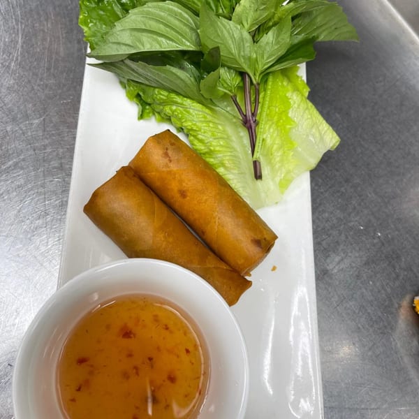 Two crispy spring rolls with fresh basil, lettuce, and a side of sweet chili dipping sauce.